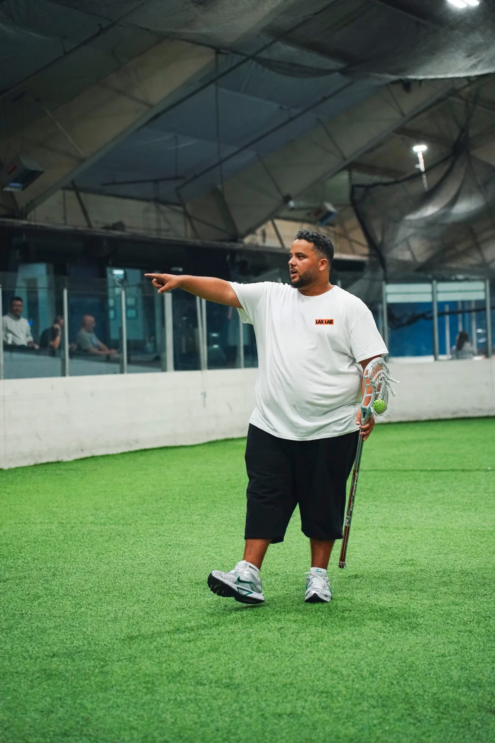 Dylan Heningburg holding a lacrosse stick and coaching on the indoor field