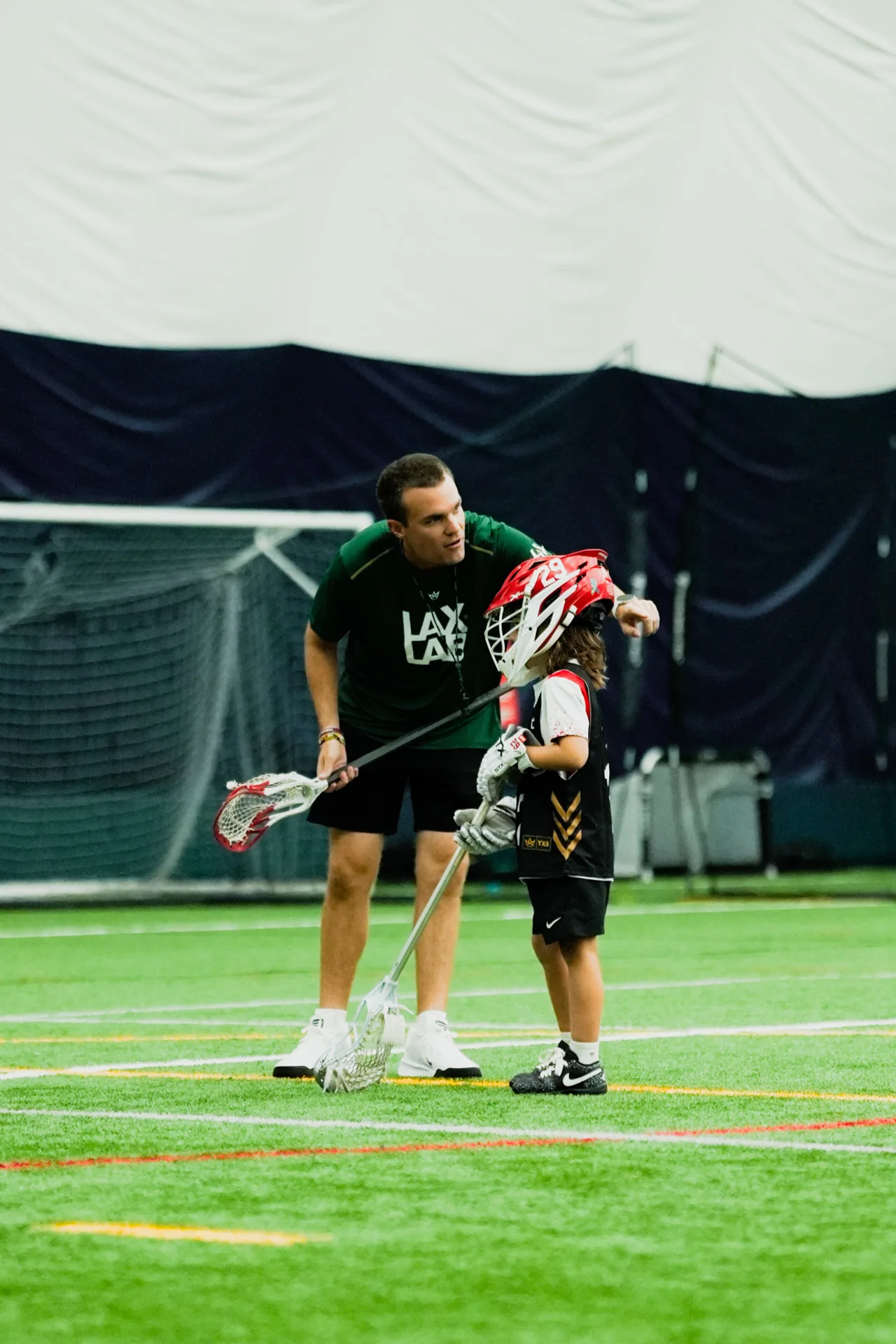 A coach works with a player beside a lacrosse goal