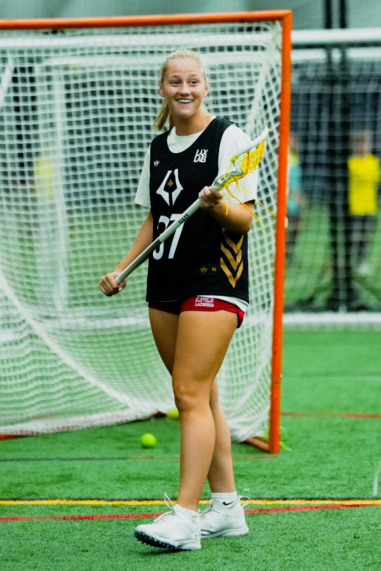 A lacrosse player holds her stick beside the goal