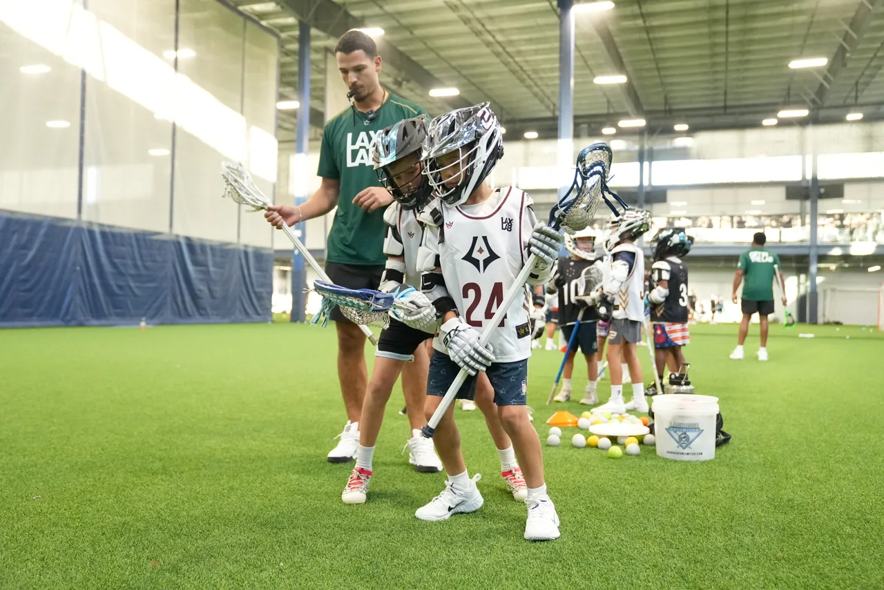 A young lacrosse player practices with a coach