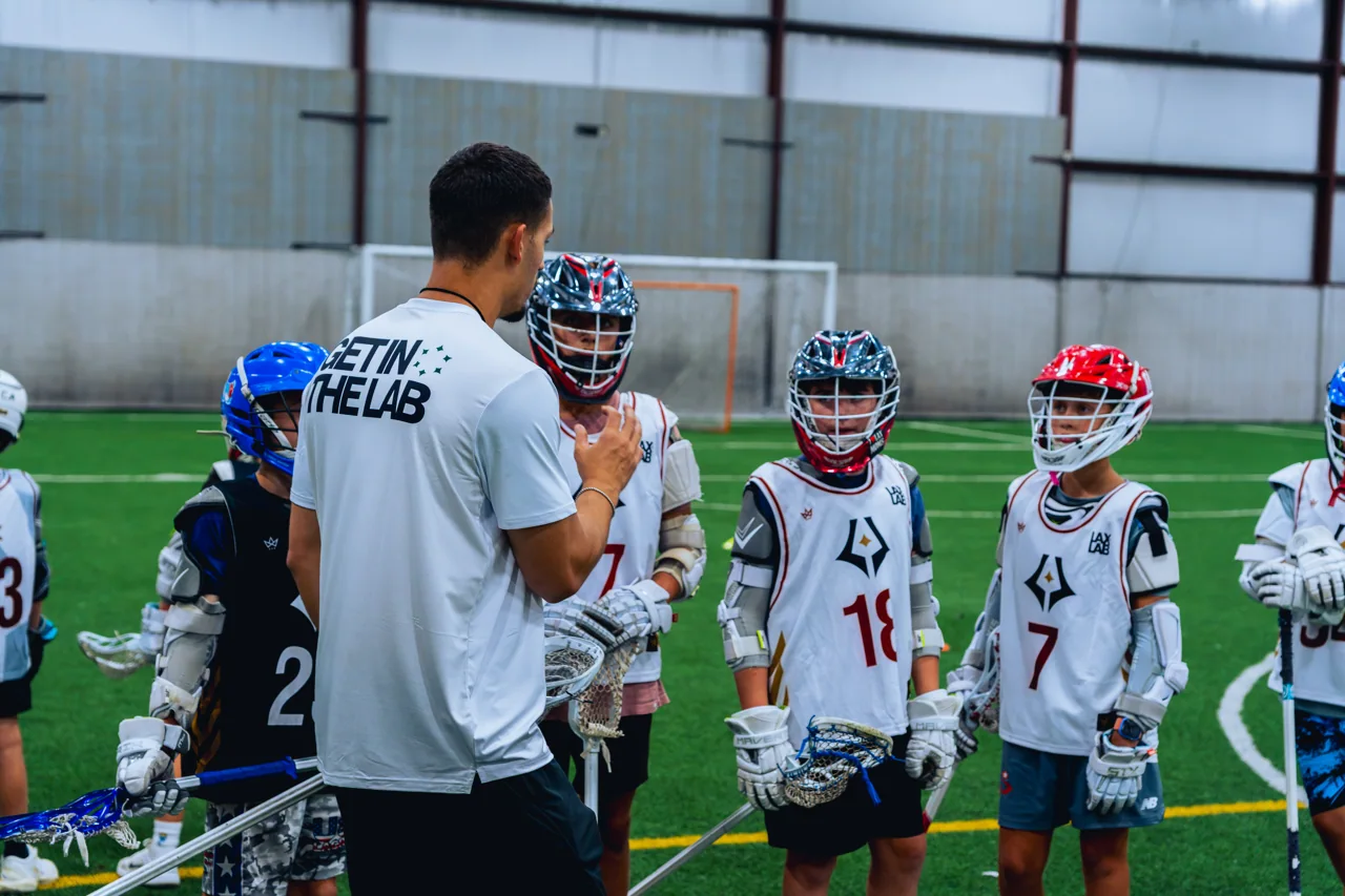 A coach gives a group of young players instruction during indoor lacrosse training