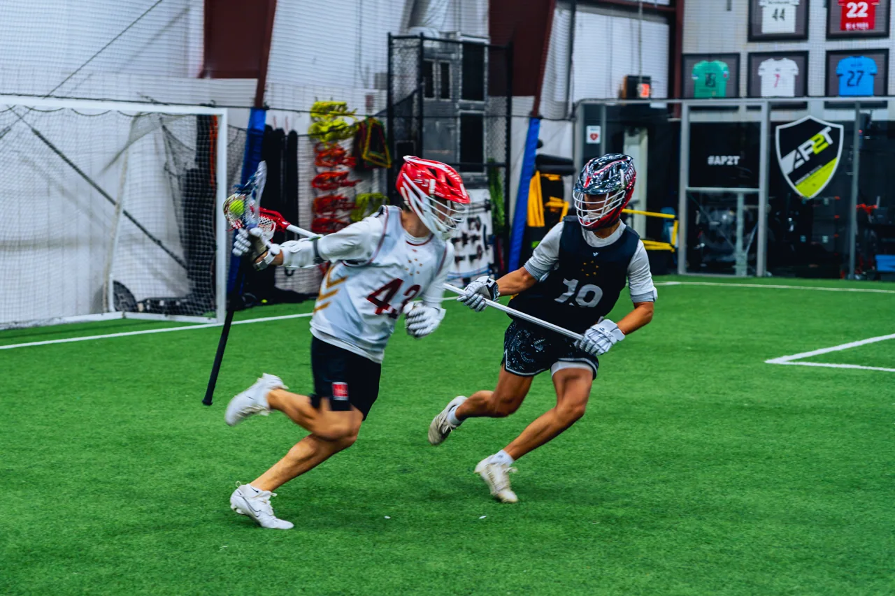 Two lacrosse players compete for position on the indoor field